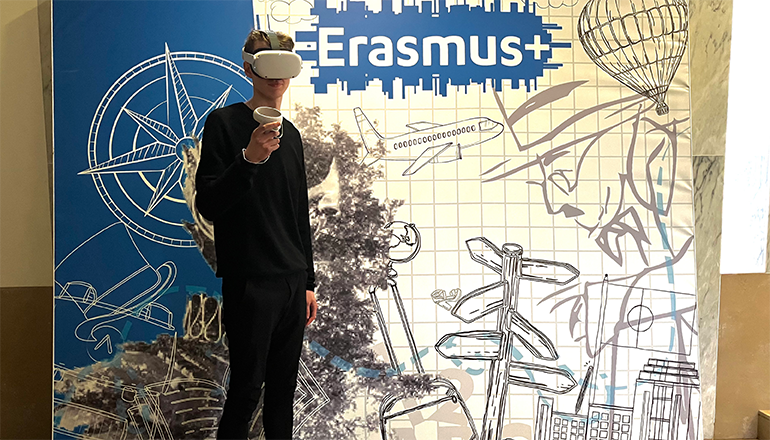 Kille med VR-glasögon står framför en bildbakgrund med texten Erasmus+.