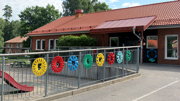 Staket med färgglada cirklar i förgrunden, röd skolbyggnad i bakgrunden.