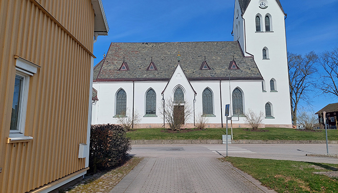 Utfart mitt emot kyrkan där sikten åt vänster är skymt av en häck.